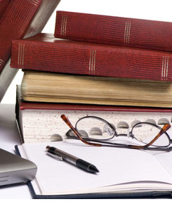 Imagen de unas gafas y un bolígrafo situados al lado de libros con documentación financiera.