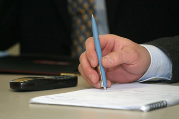 Imagen de la mano de un ejecutivo sosteniendo un bolígrafo sobre un cuaderno con anotaciones.